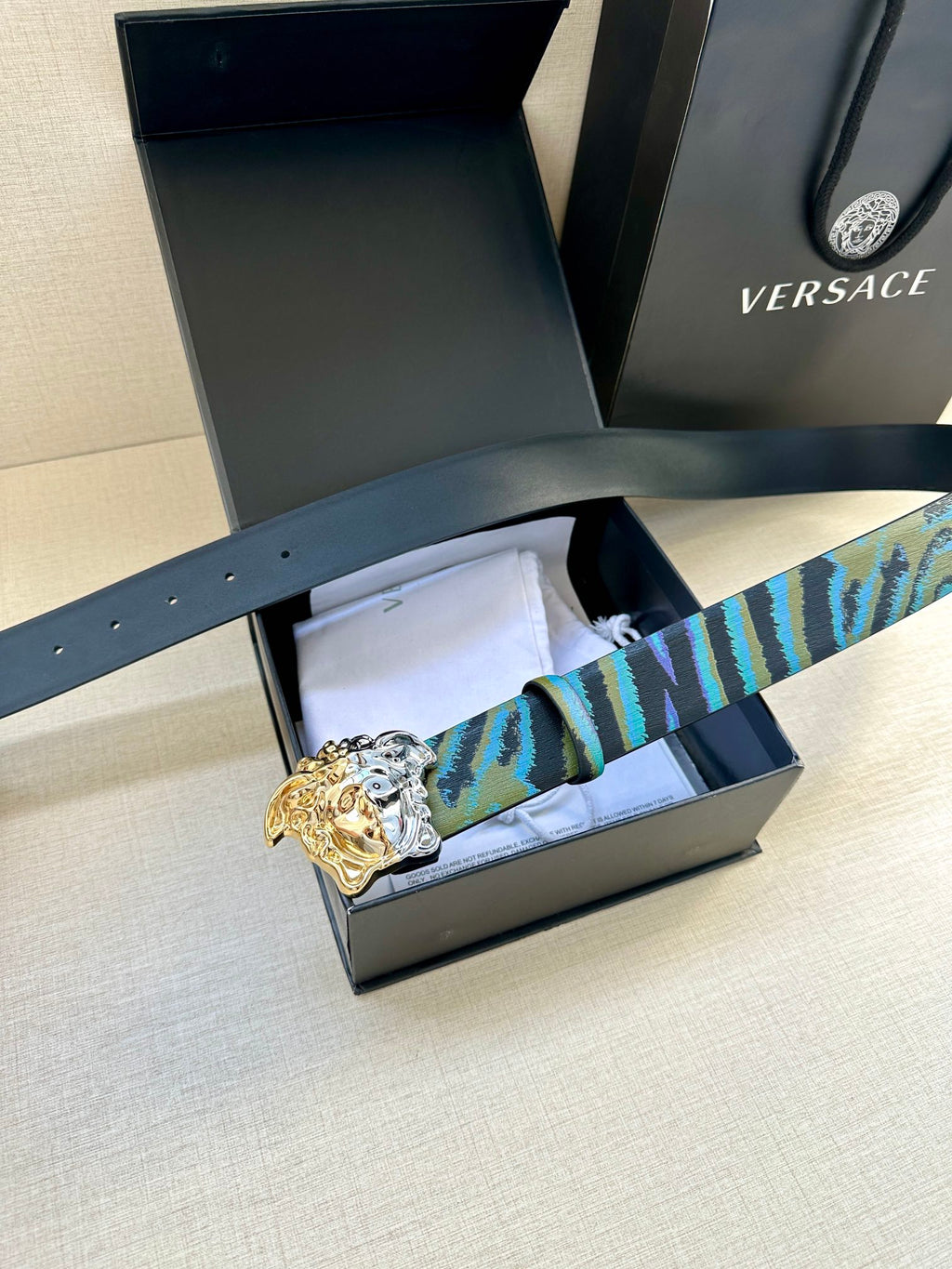Flat-lay belt in blue, teal and purple patterned strap with Medusa gold-silver buckle