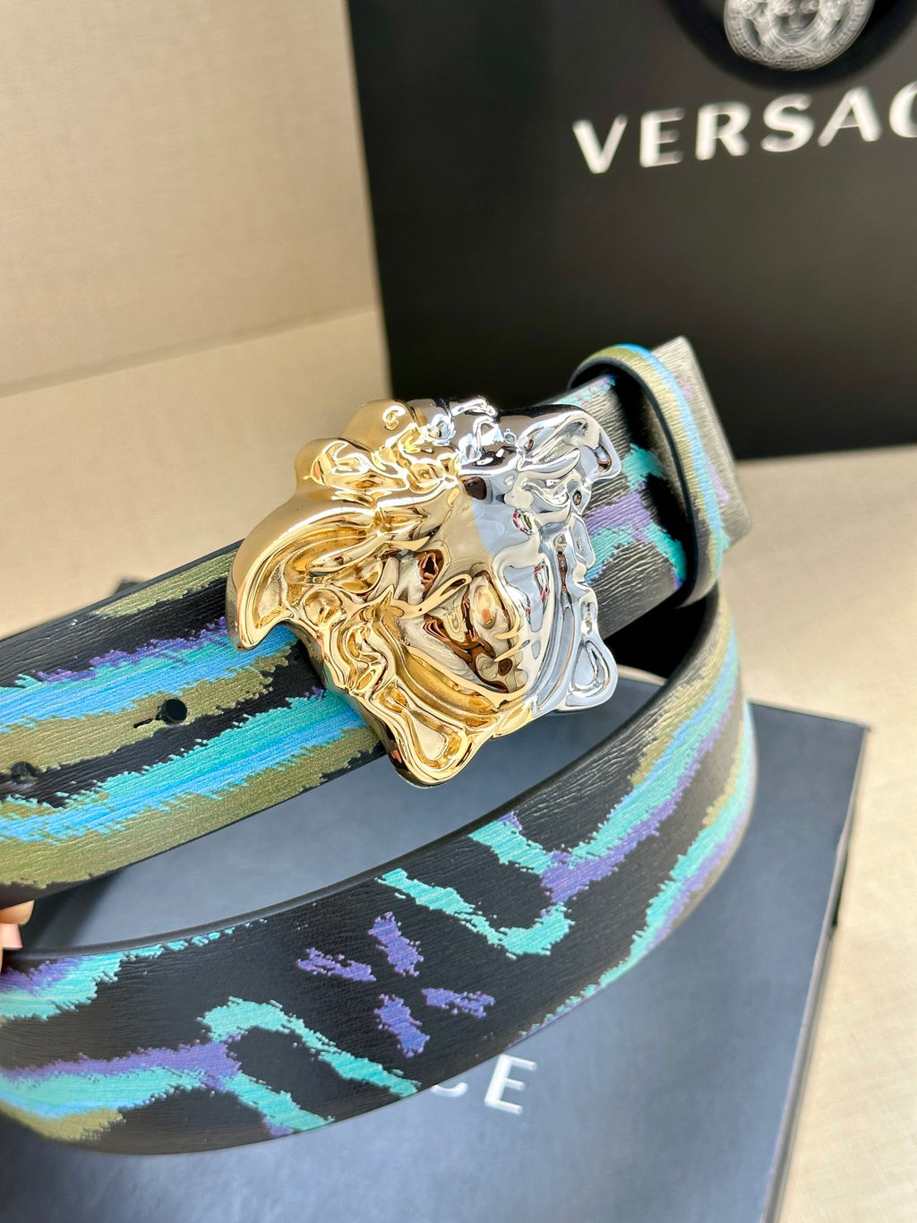 Close-up of blue leather belt with teal stripe print and gold-and-silver Medusa buckle