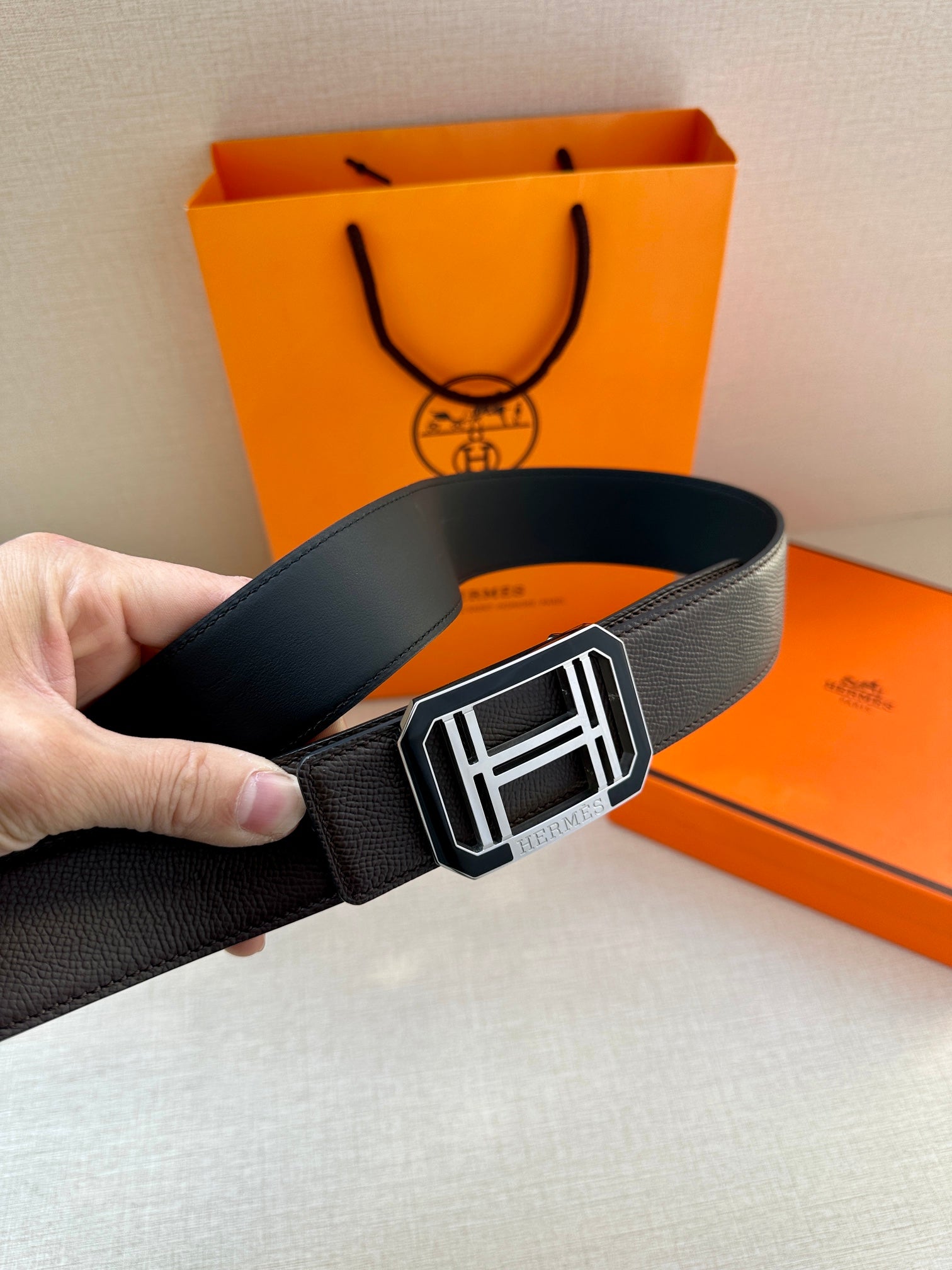 Black leather belt with large silver-tone buckle, hand holding strap