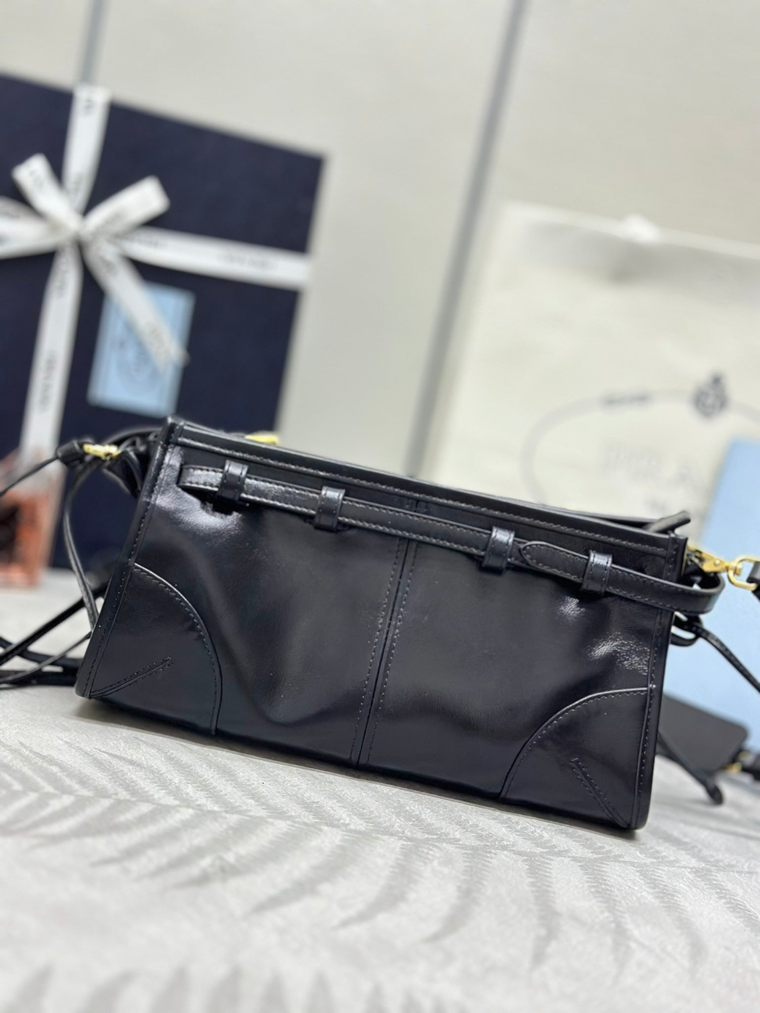 Black leather clutch-style bag with gold-tone buckle strap and front logo plaque