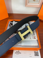Blue leather belt with textured finish and large gold-tone H buckle centerpiece