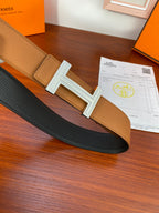 Two-tone leather belt with tan and dark straps and silver H buckle centerpiece.