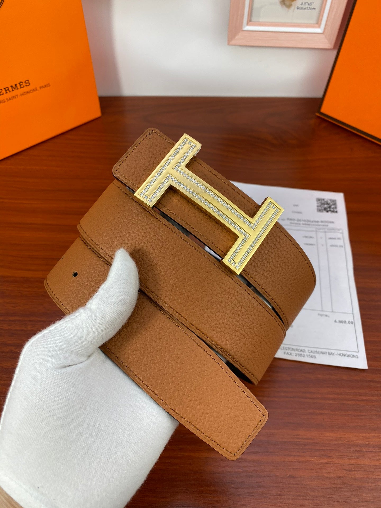 Reversible leather belt with tan strap and silver H buckle on dark keeper tab.