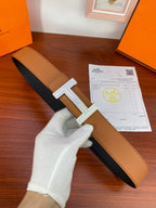 Reversible leather belt with tan and dark sides and silver H buckle detail.