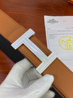 Reversible belt buckle: silver H with engraved border on tan leather strap.