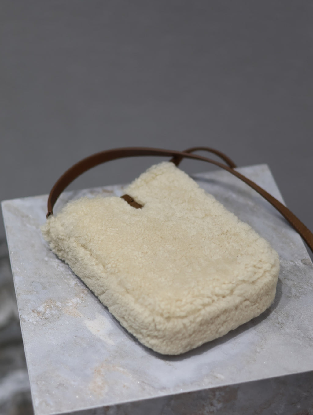 Cream shearling-style crossbody bag with brown leather shoulder strap loop