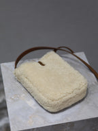 Cream shearling-style crossbody bag with brown leather shoulder strap loop