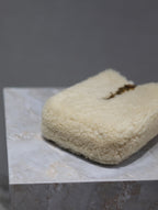 Cream shearling-style pouch bag with curved shape and brown leather strap
