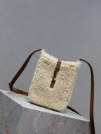 Cream shearling-style bucket bag with brown leather trim and shoulder strap