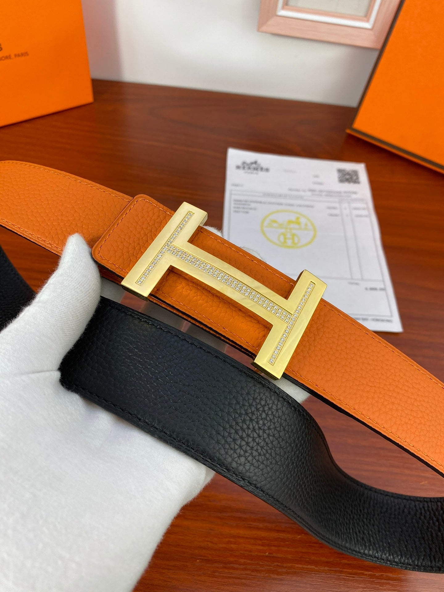 Reversible leather belt showing orange strap and black reverse, silver H buckle