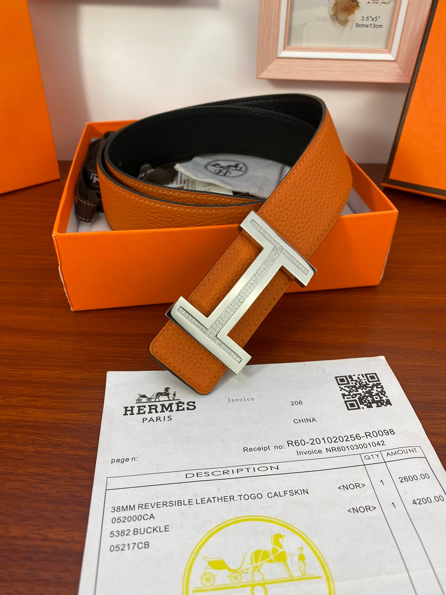 Reversible leather belt in box with orange strap and black reverse, silver H buckle