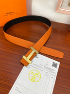 Reversible leather belt with orange strap and silver H buckle lying flat