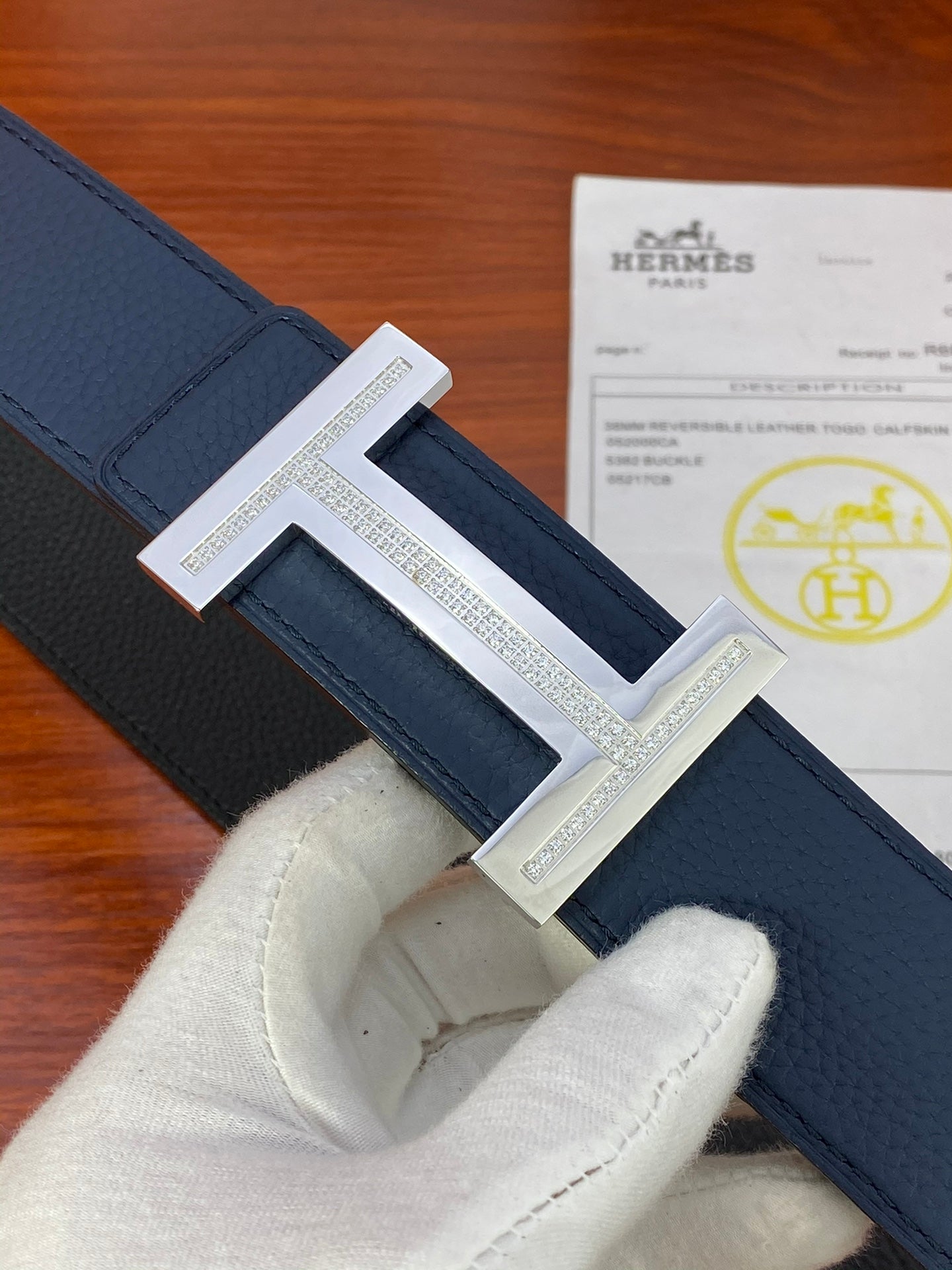 Hermès belt close-up: dark blue strap with silver-tone rectangular H buckle.