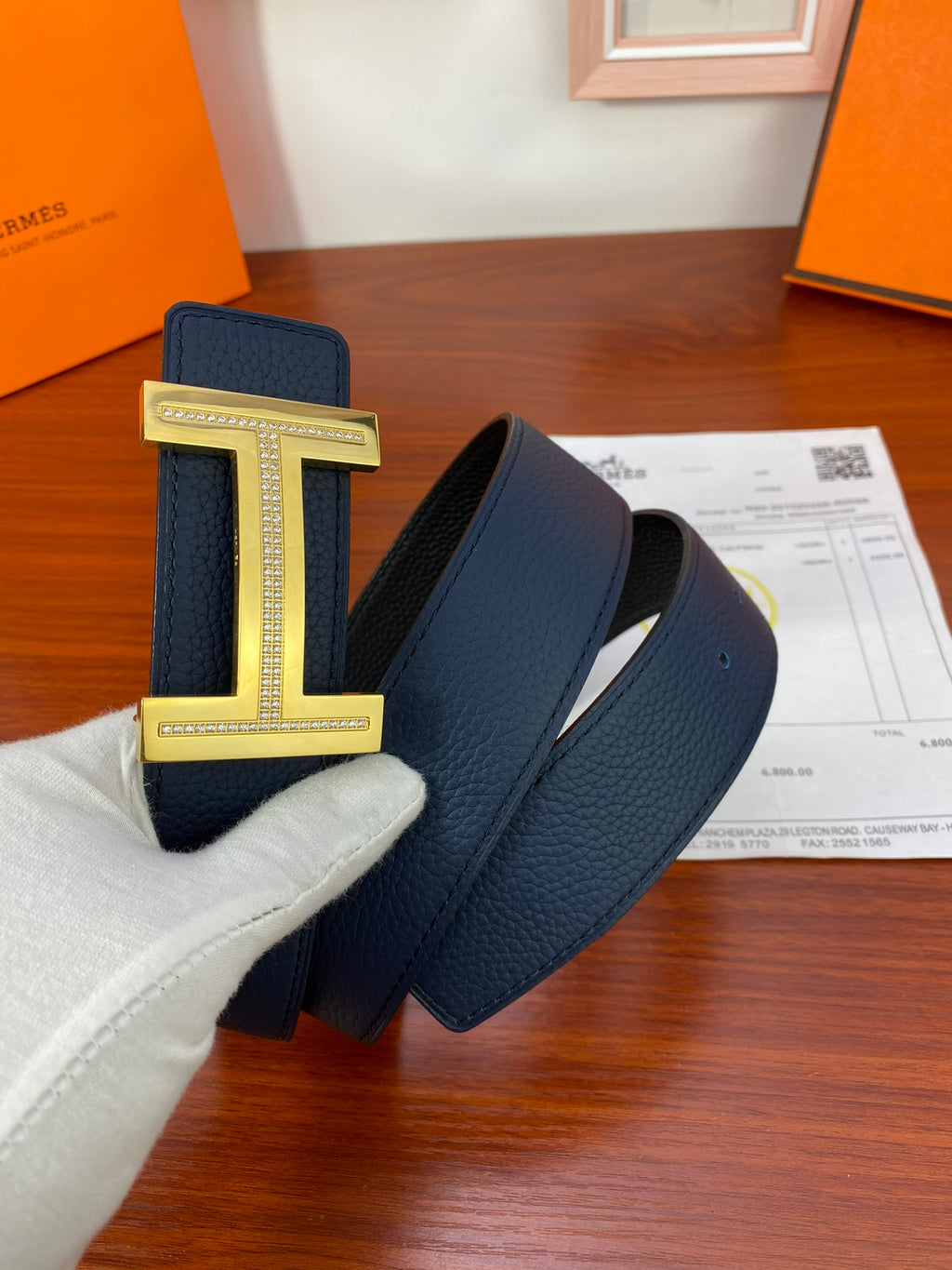 Hermès belt with dark blue leather strap and gold-tone H buckle.