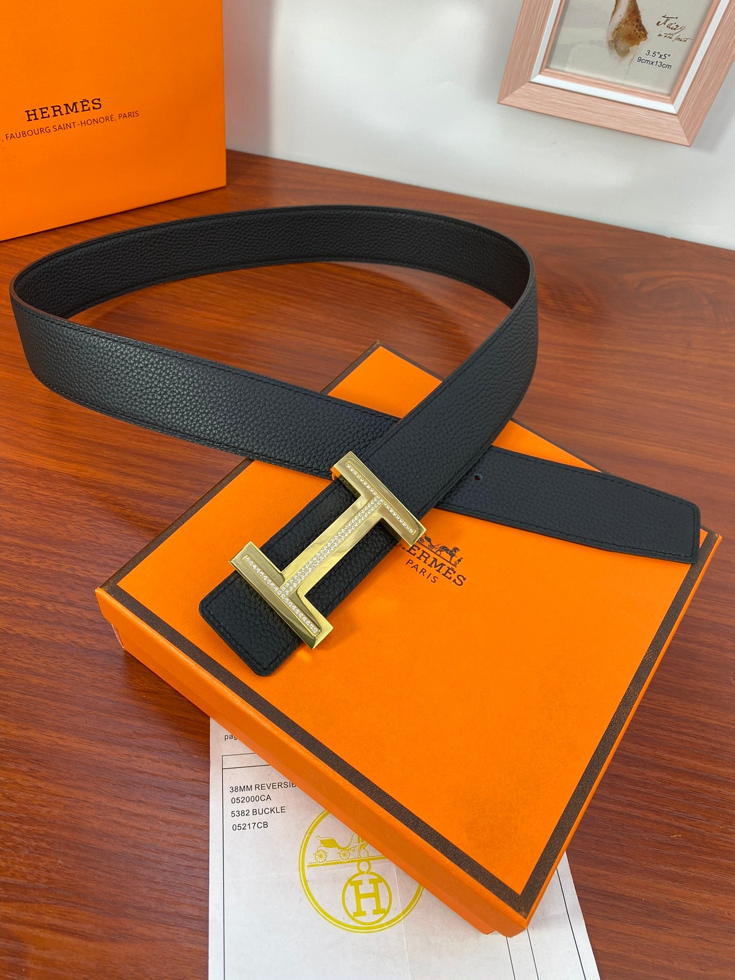 Black leather belt with gold H buckle, looped around gift box
