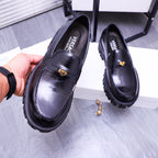 Black Versace leather loafers with gold emblem strap and chunky tread sole, held up