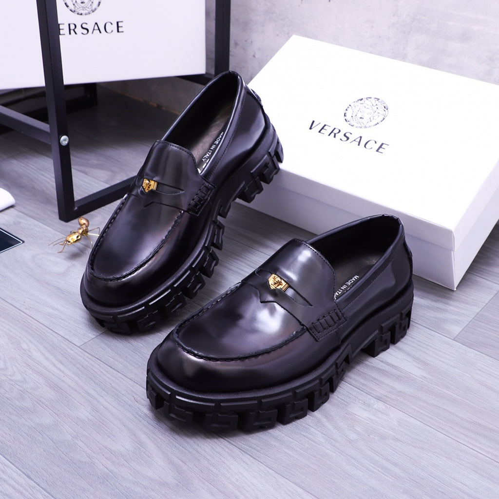 Pair of black Versace leather loafers with gold emblem and rugged lug soles, angled view