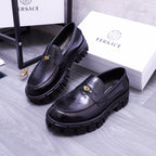 Pair of black Versace leather loafers with gold emblem and rugged lug soles, angled view
