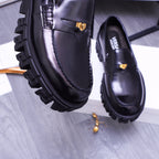 Close-up of black Versace loafer with gold emblem and stitched strap, chunky lug sole