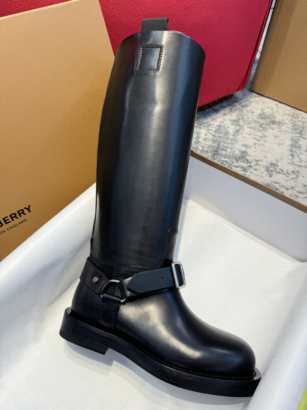 Black knee-high leather boot with a single front buckle strap and flat sole