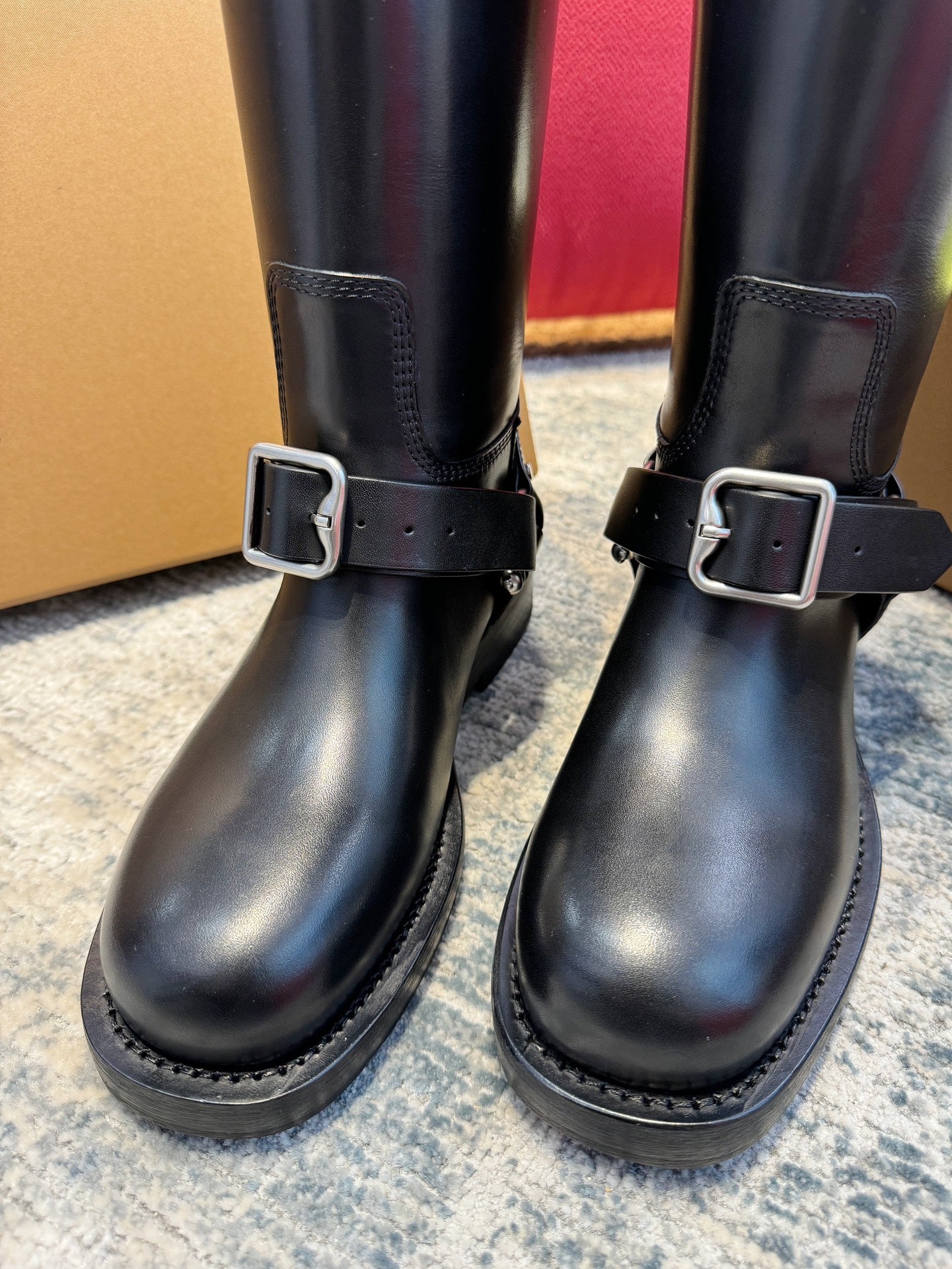 Close-up of black knee-high boots with metal buckle straps and stitched panels