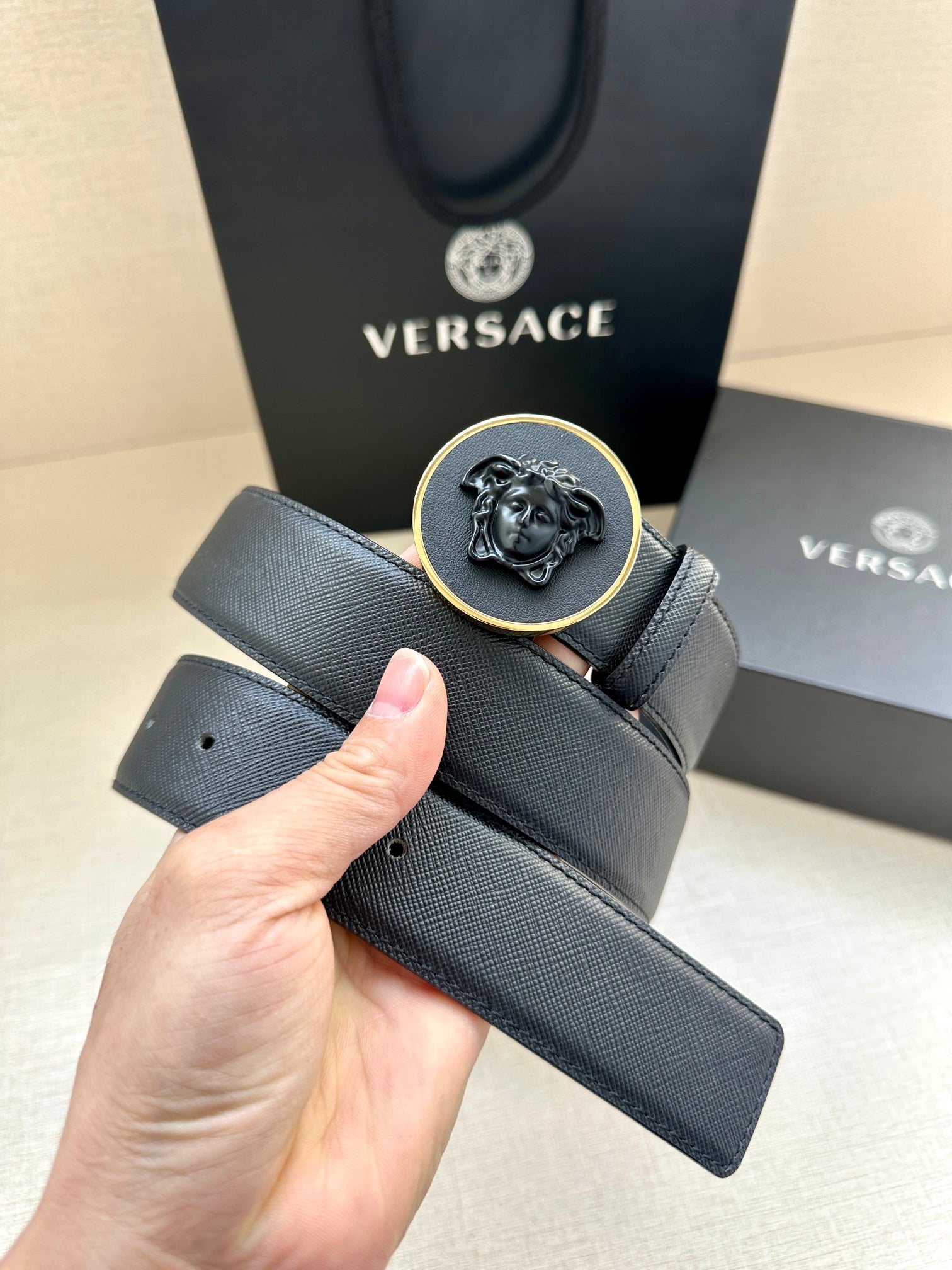 Versace dark blue leather belt held by hand, round Medusa buckle and belt holes