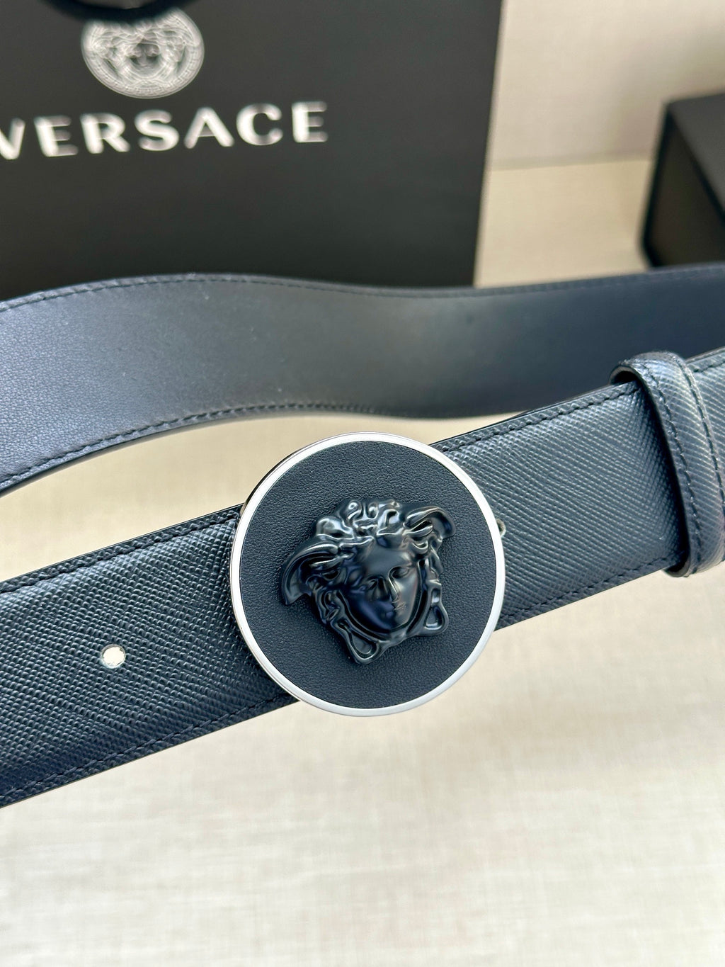 Versace dark blue leather belt close-up of round Medusa buckle and strap texture