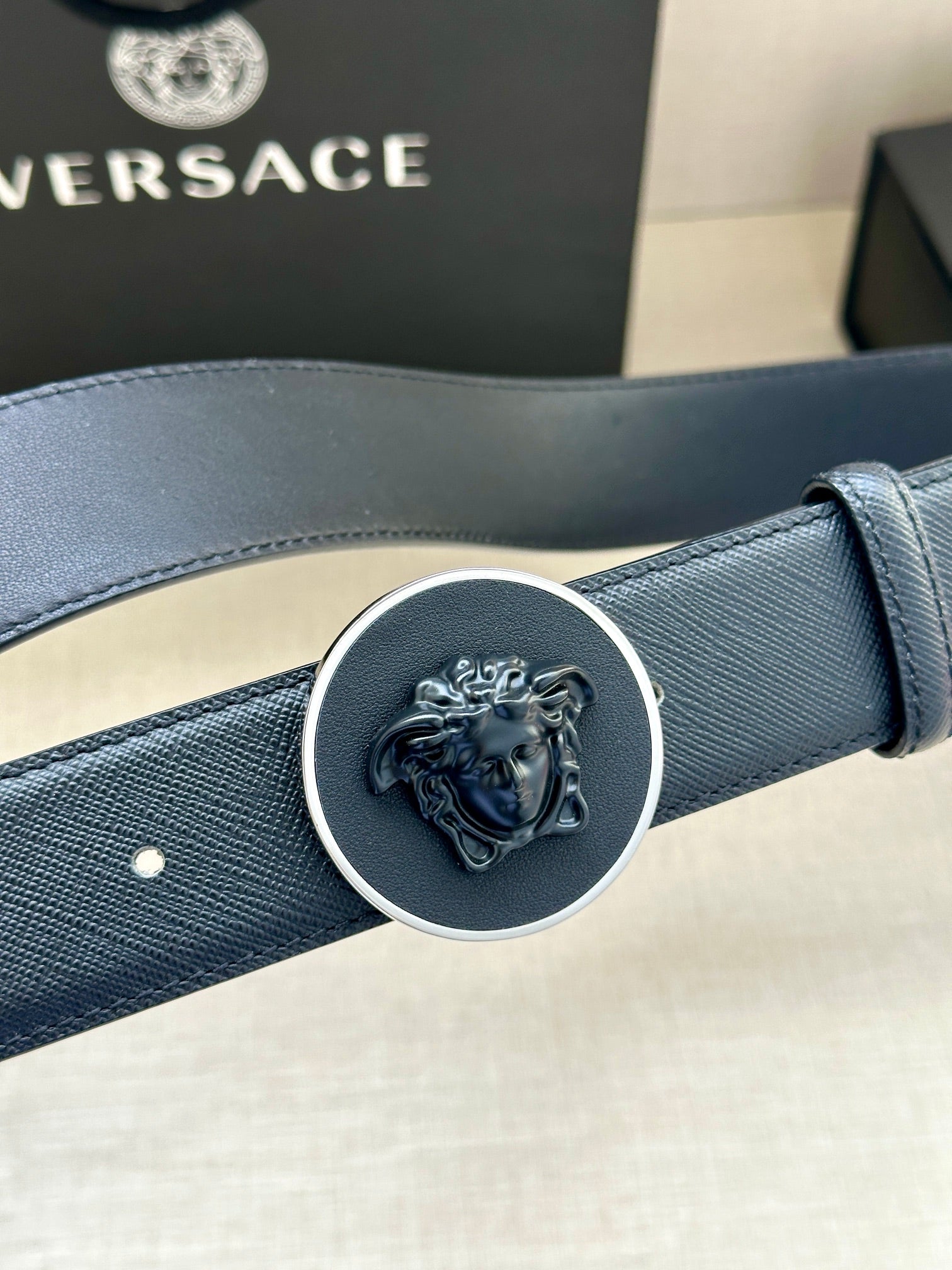 Versace dark blue leather belt close-up of round Medusa buckle and strap texture