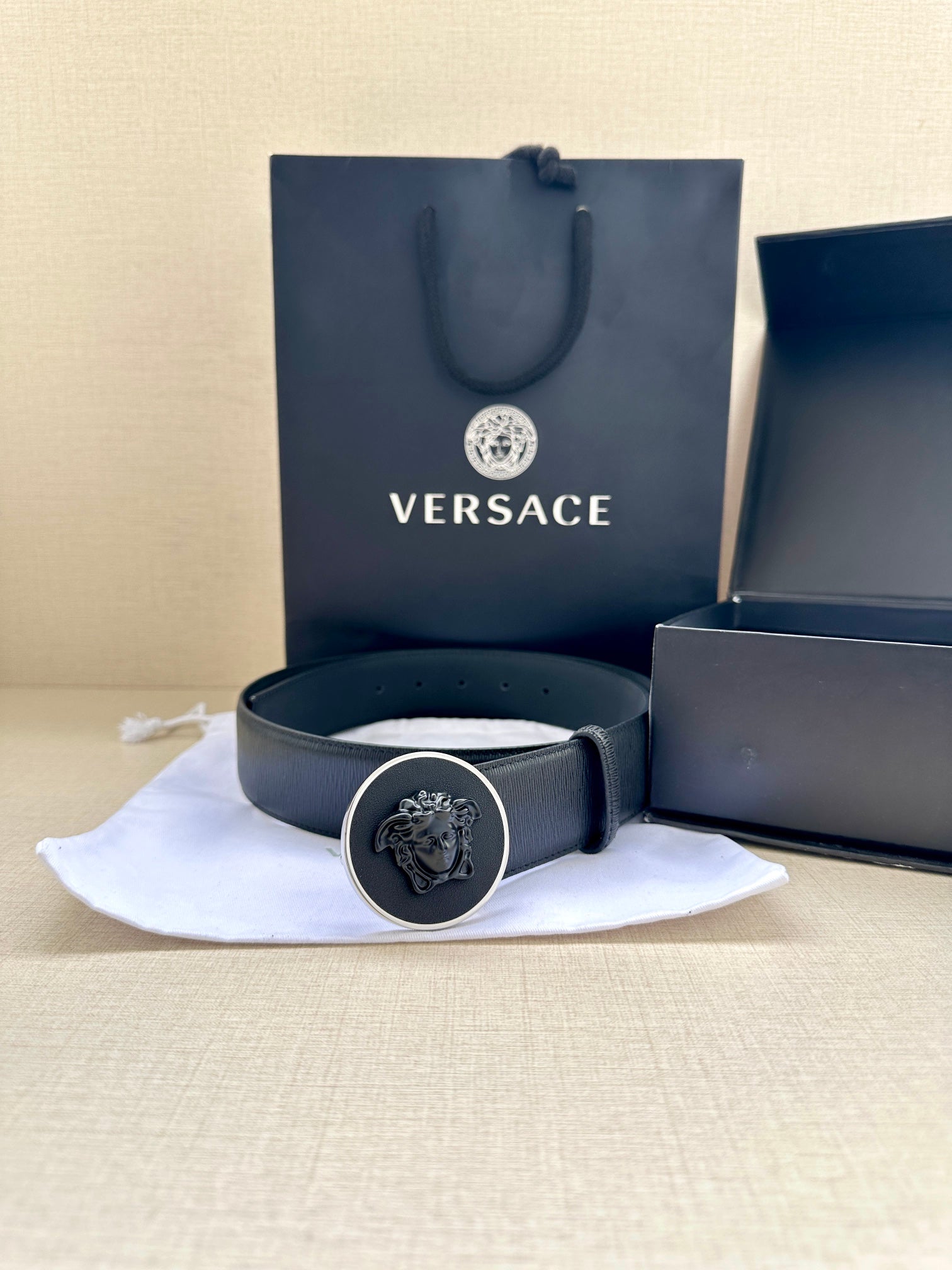 Versace belt with gold-tone emblem buckle on folded cloth, dark blue strap