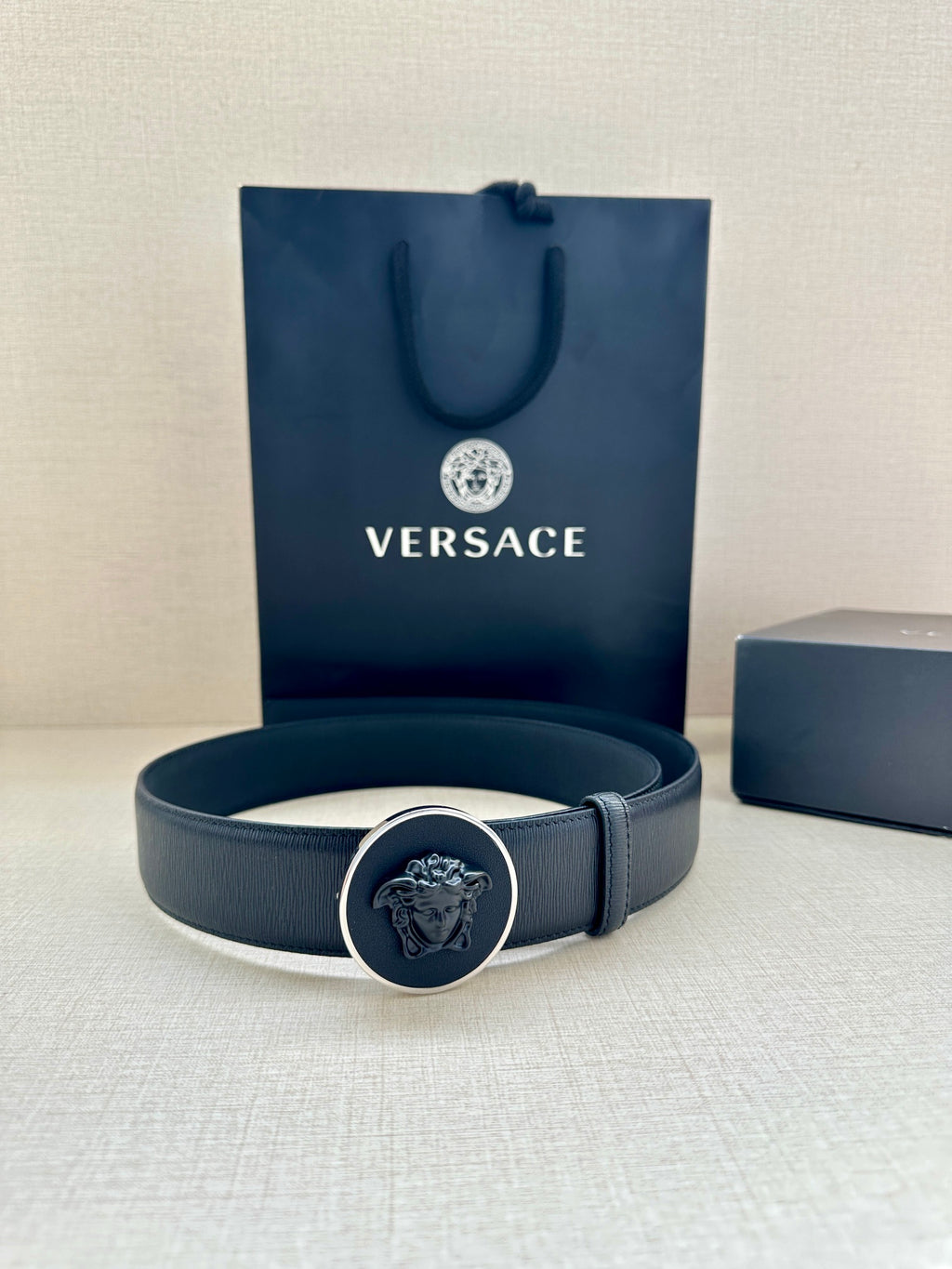 Versace belt laid flat with gold-tone emblem buckle and dark blue strap