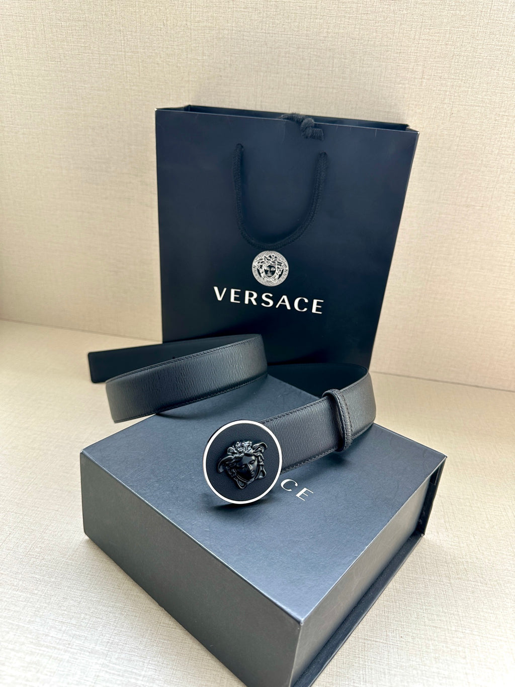 Versace belt displayed with dark blue strap and round emblem buckle