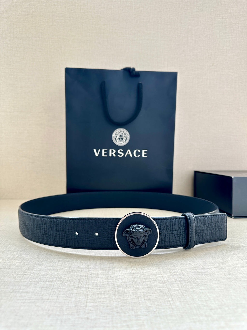 Dark blue leather-look belt with round logo buckle and punched holes