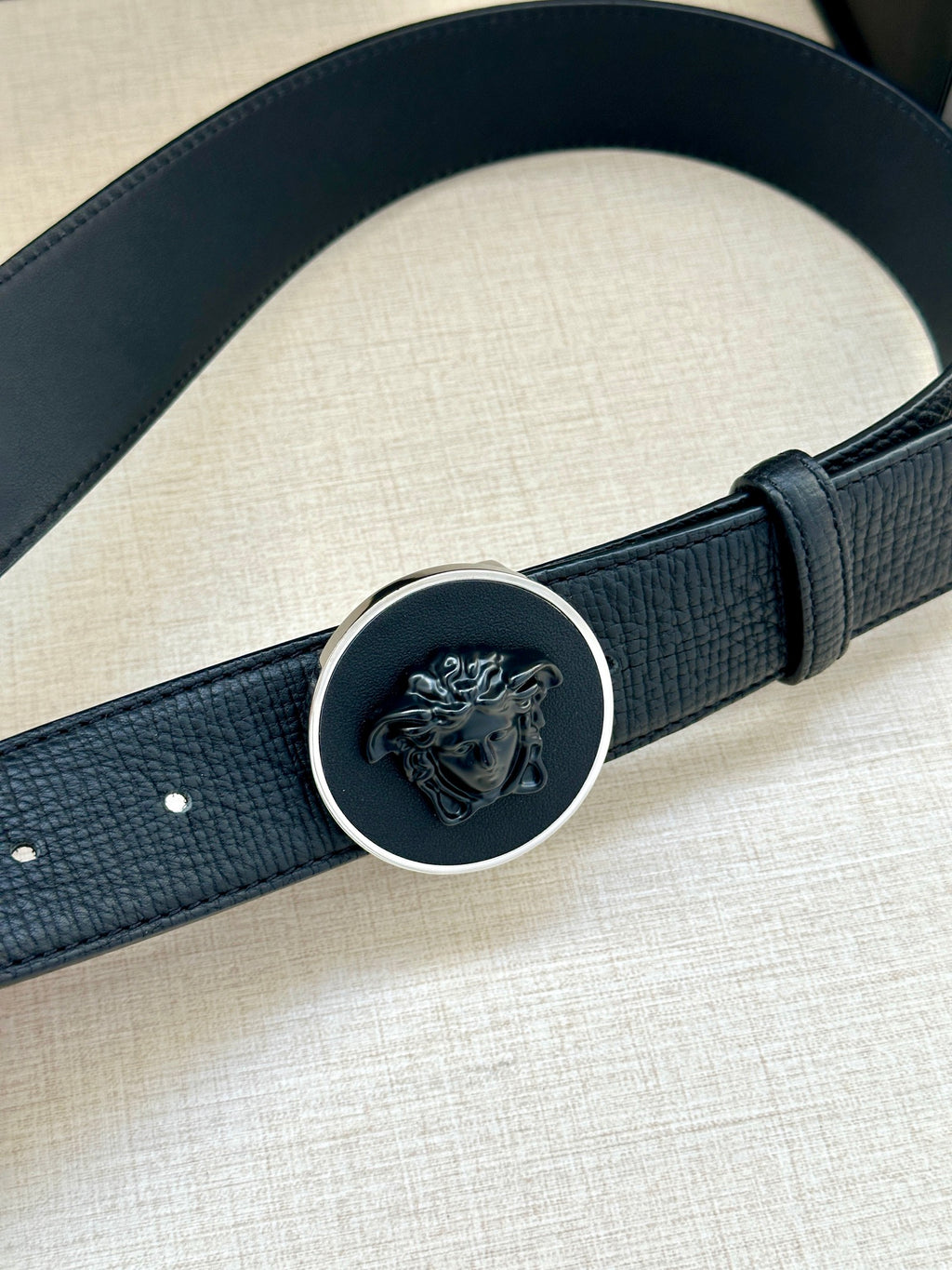 Close-up of dark blue leather-look belt with round logo buckle and metal rim