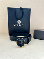 Dark blue leather-look belt with round logo buckle in front of a box