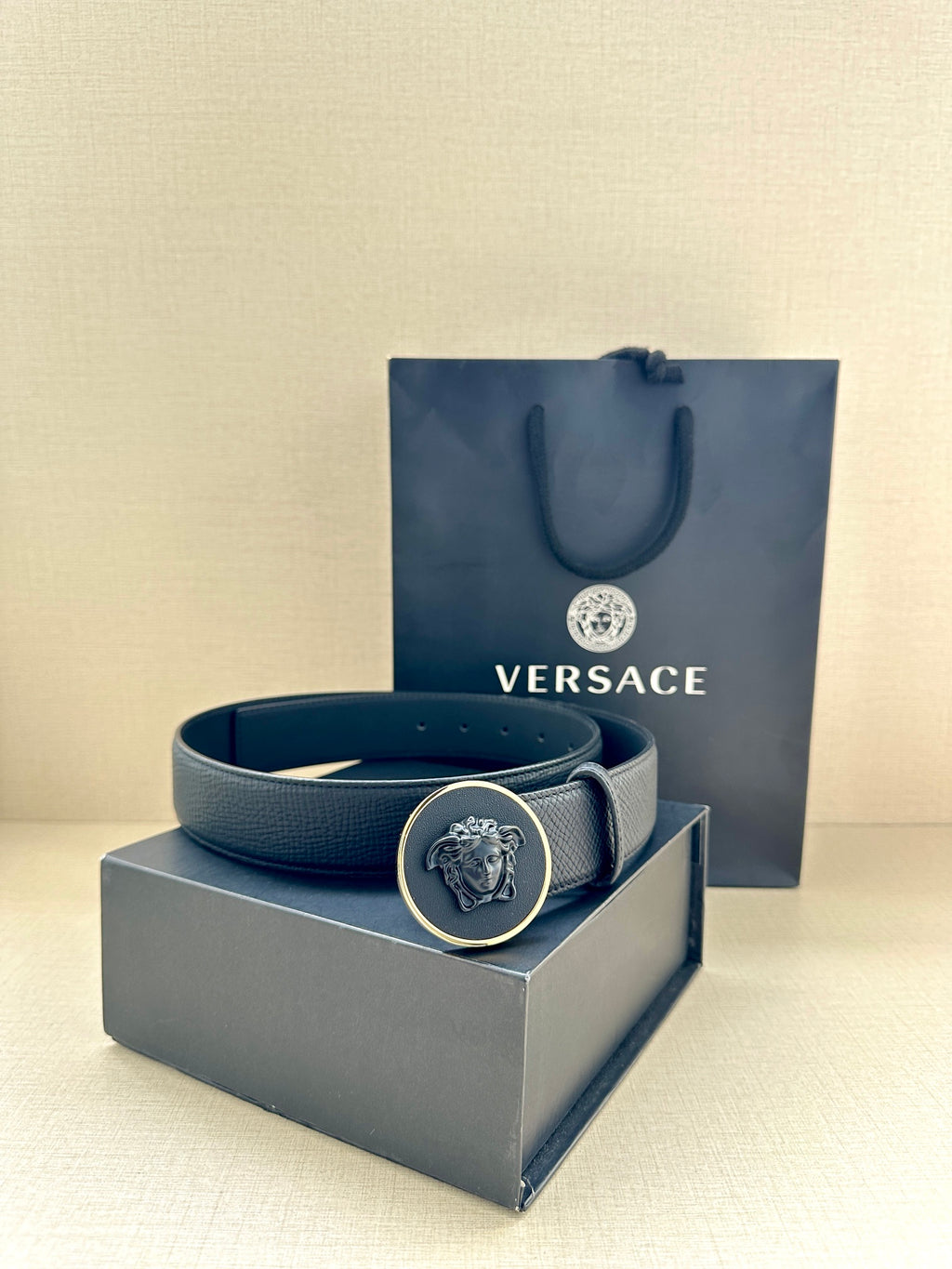 Dark blue leather-look belt with round logo buckle resting on gift box