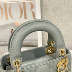 Dior mini handbag handle close-up in light blue-gray leather with gold rings and stitching.