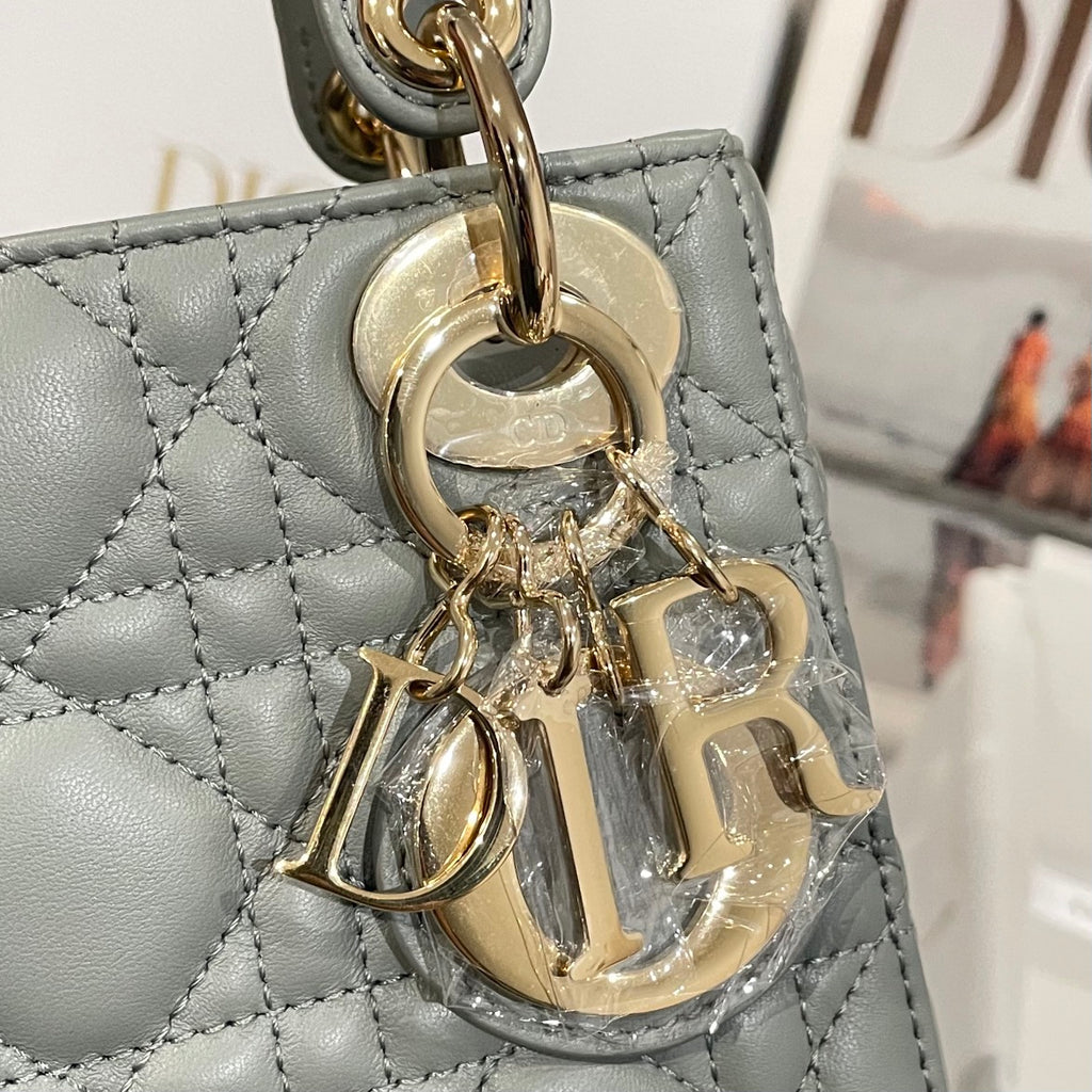 Dior handbag charm and gold hardware on light blue-gray quilted leather panel.