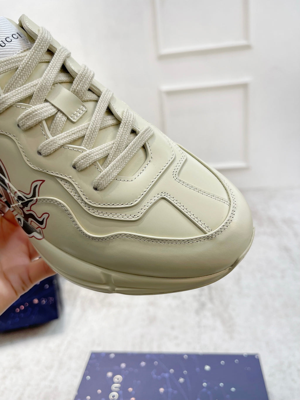 Gucci unisex luxury sneaker close-up, cream laces and side flame emblem