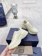 Cream Gucci unisex sneakers on shoebox, angled pair with contrast stitching