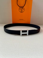 Hermes dark leather belt with silver H buckle lying on light surface
