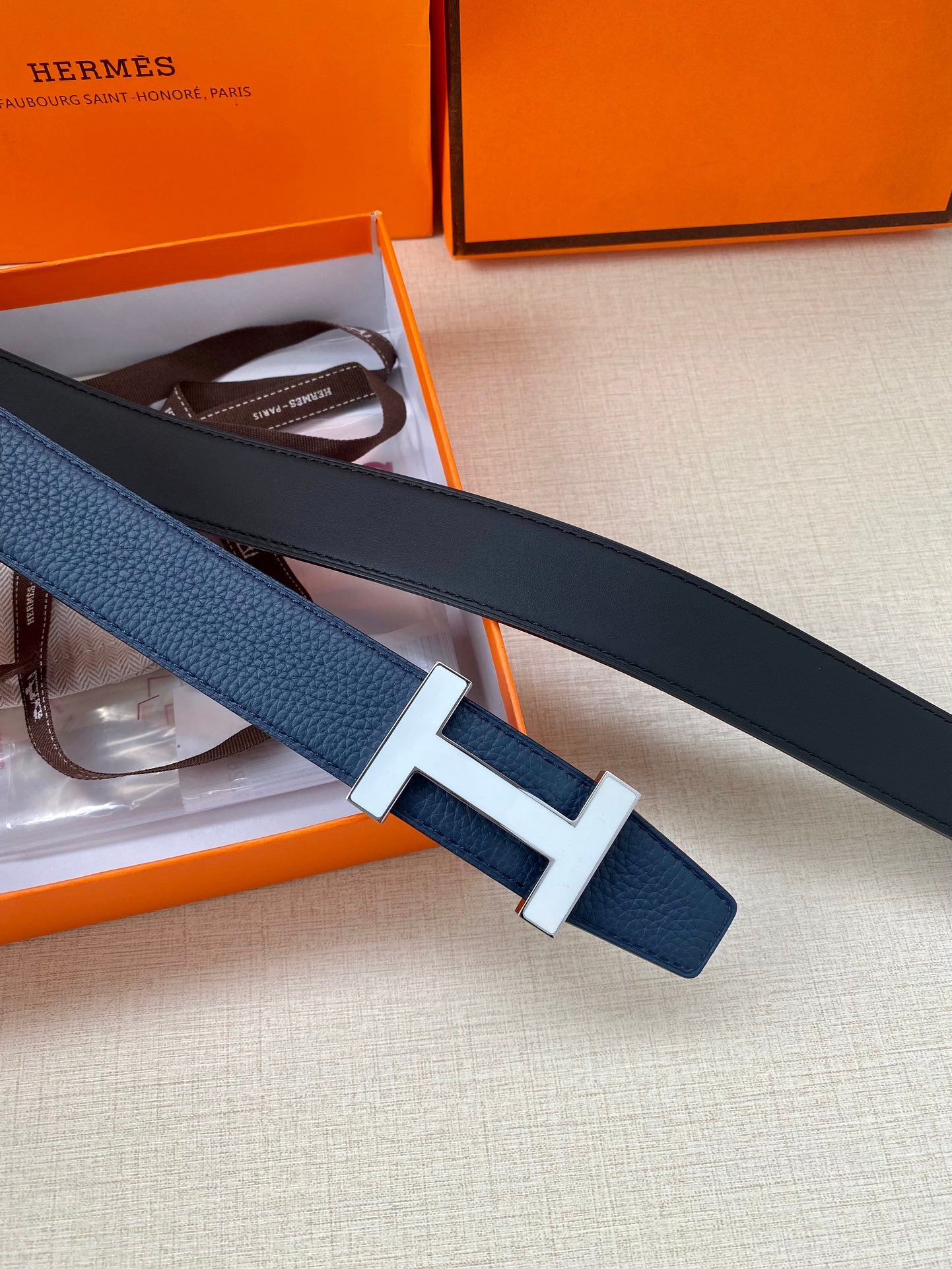 Blue leather belt with silver H buckle, stacked with a dark strap in box.