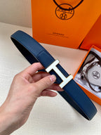 Blue leather belt with silver H buckle detail, shown held in hand.