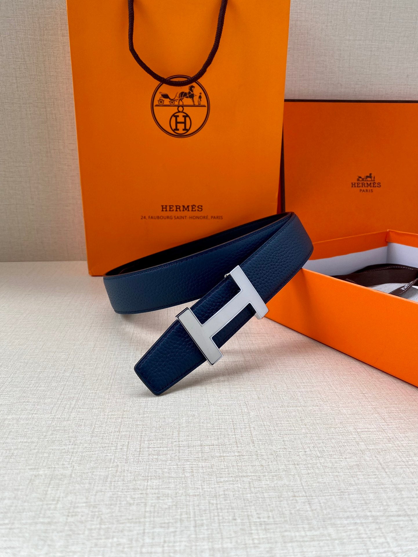 Blue leather belt with silver H buckle, styled on a surface with boxes.