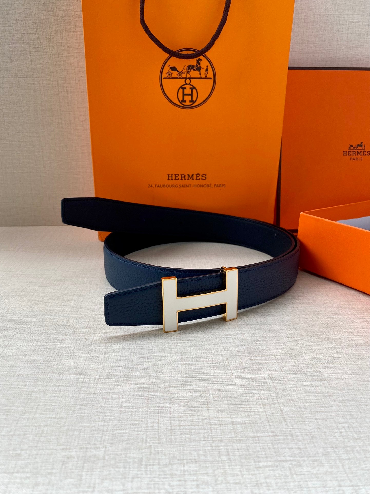 Blue leather belt with silver H buckle, laid flat on a surface.