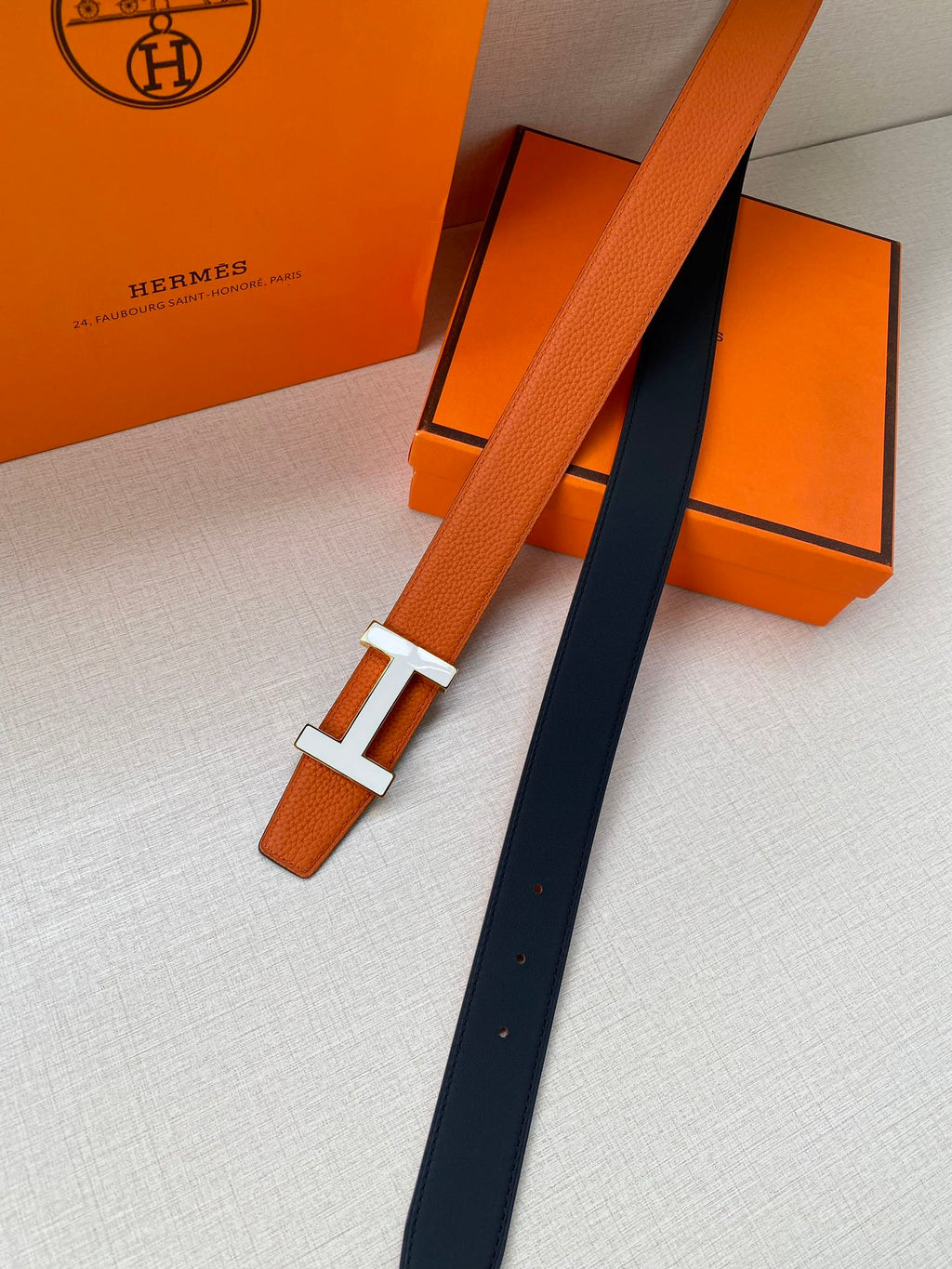 Hermes belt laid flat: orange leather with silver H buckle and dark strap