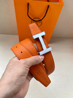 Hermes belt close-up: orange leather strap with silver H buckle and keeper tab