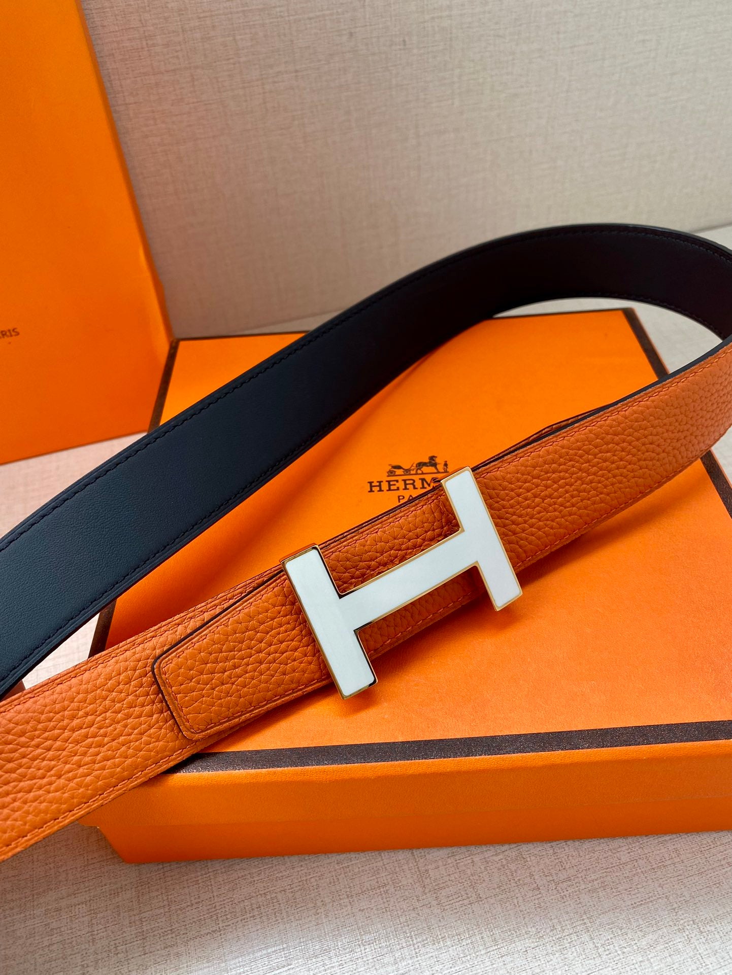 Hermes belt detail: orange leather with silver H buckle and dark blue underside