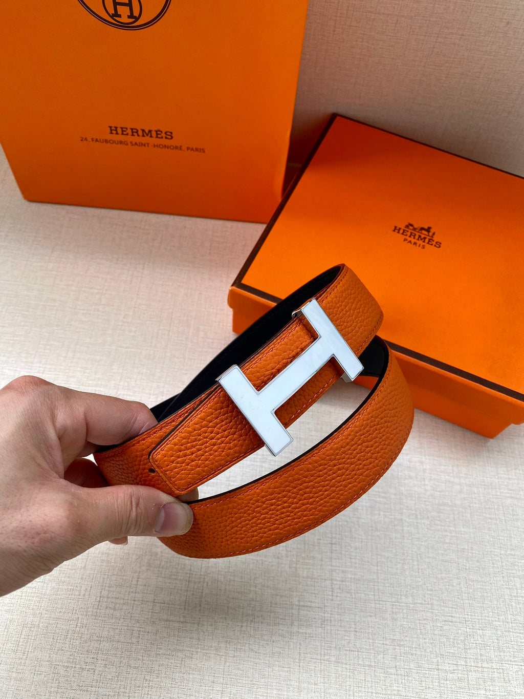 Hermes belt buckle close-up: orange leather with silver H and center bar