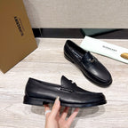 Black leather loafer with side strap detail and stitched toe, laid on floor