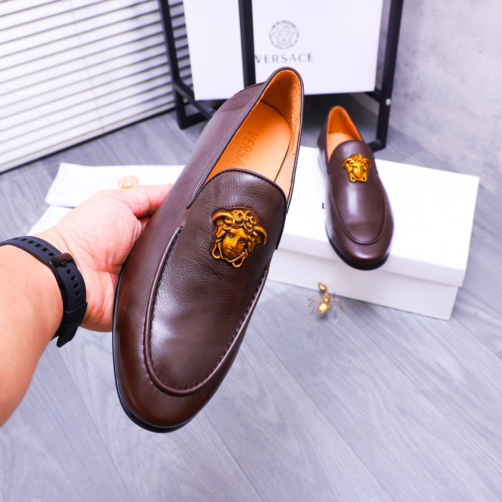 Brown leather slip-on loafer held in hand, gold Medusa emblem